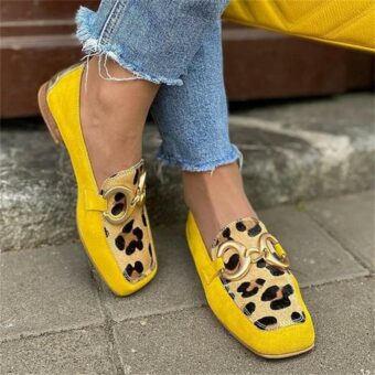 Kvinna står på gatan i jeans och gula och leopardfärgade loafers med fyrkantig tå