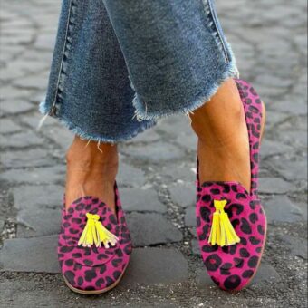 Kvinna som står med benen i kors på gatan i jeans och rosa loafers med tofsar och leopardmönster