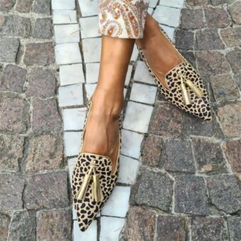 Kvinna på gatan med korslagda ben iförd guld leopard loafers med spetsig tå